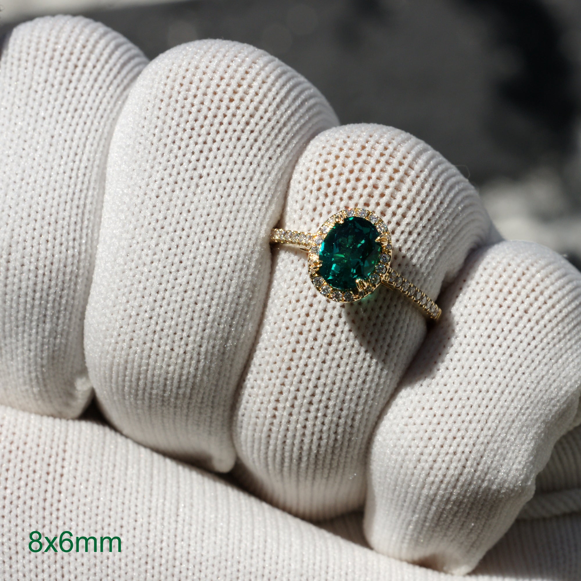 Oval cut green emerald engagement ring with a diamond halo in yellow gold