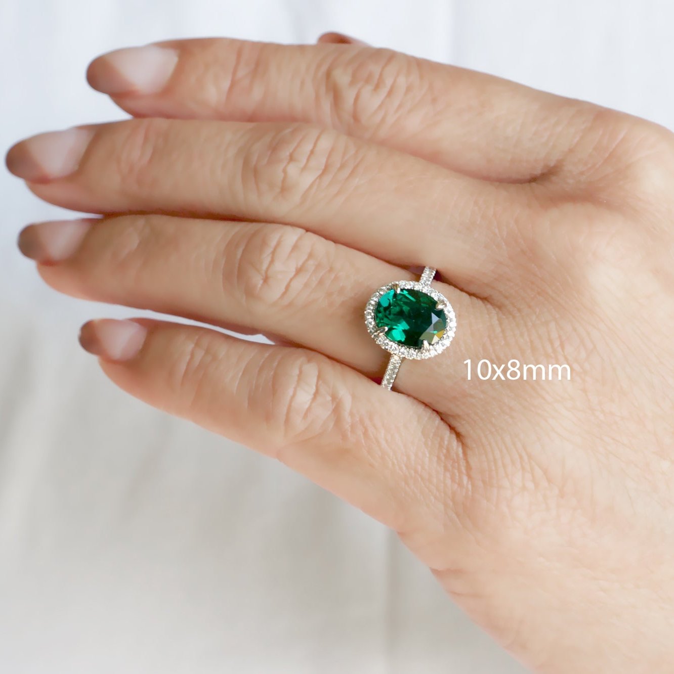 Oval cut green emerald engagement ring with a diamond halo in white gold