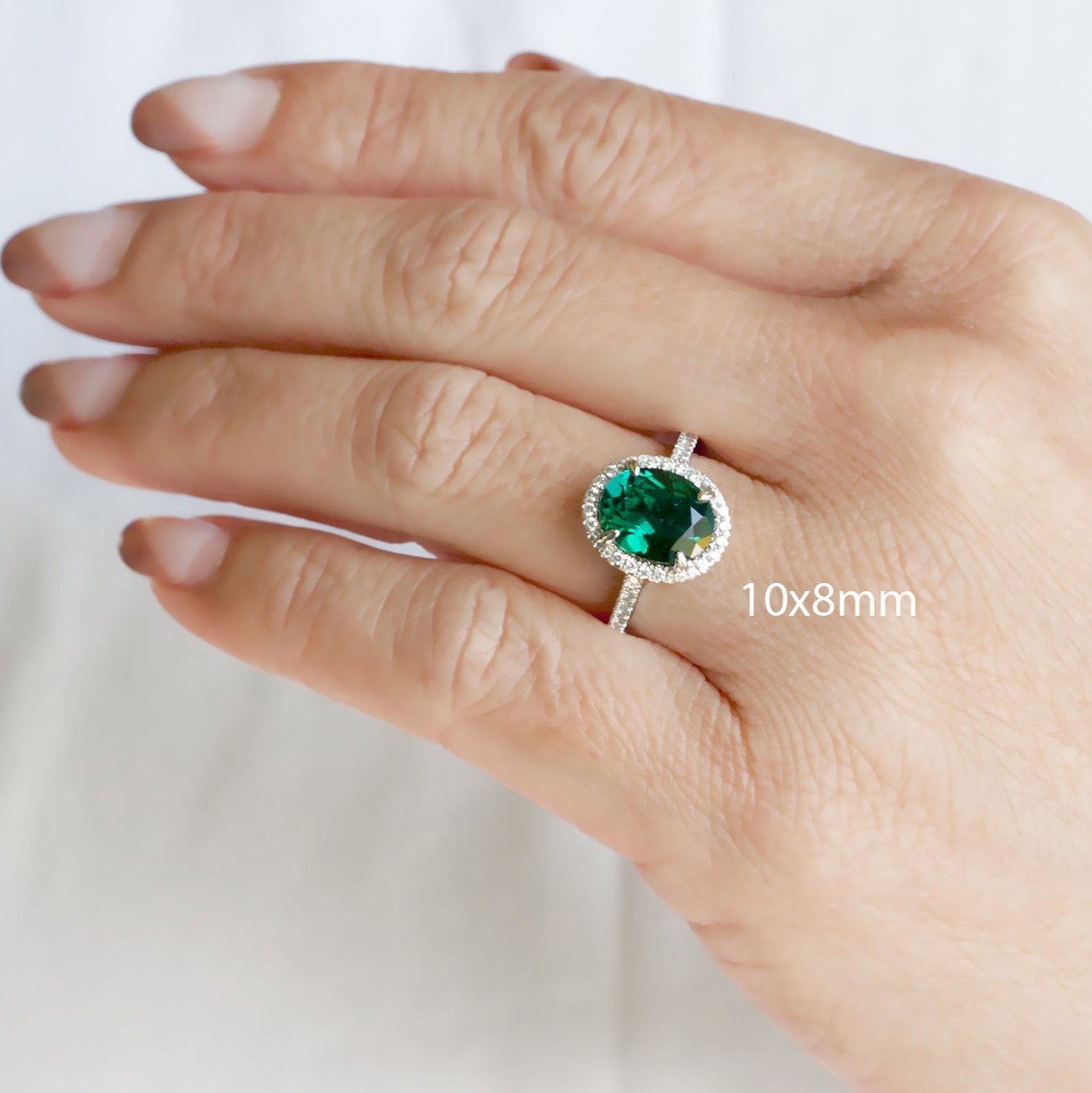 Oval cut green emerald engagement ring with a diamond halo in white gold